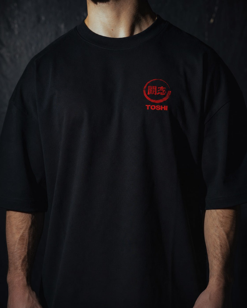 Homme de face portant un t-shirt oversize de couleur noire, avec un logo japonais rouge de la marque TOSHI inspiré des mangas et animes.