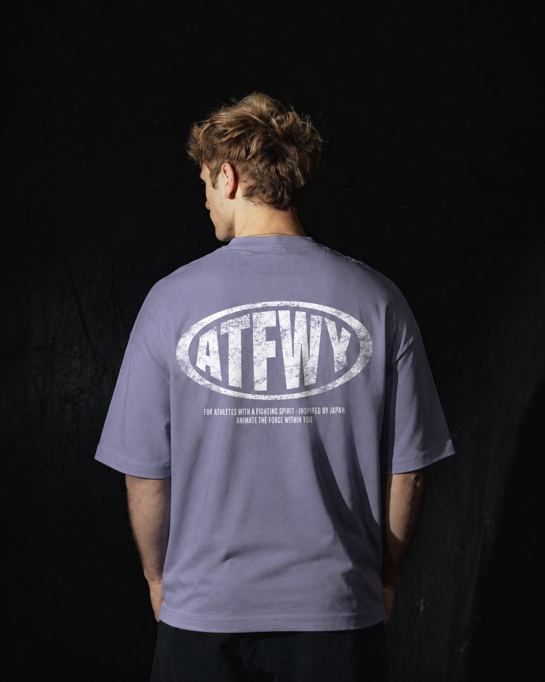 Homme de dos portant un t-shirt oversize de couleur violette, avec un visuel des lettres ATFWY en rouge, destiné aux athlètes et inspiré de la culture japonaise.