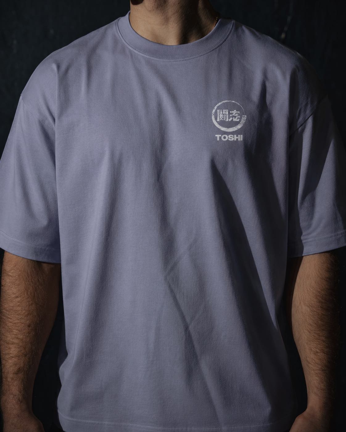 Homme de face portant un t-shirt oversize de couleur violette, avec un logo japonais rouge de la marque TOSHI inspiré des mangas et animes.
