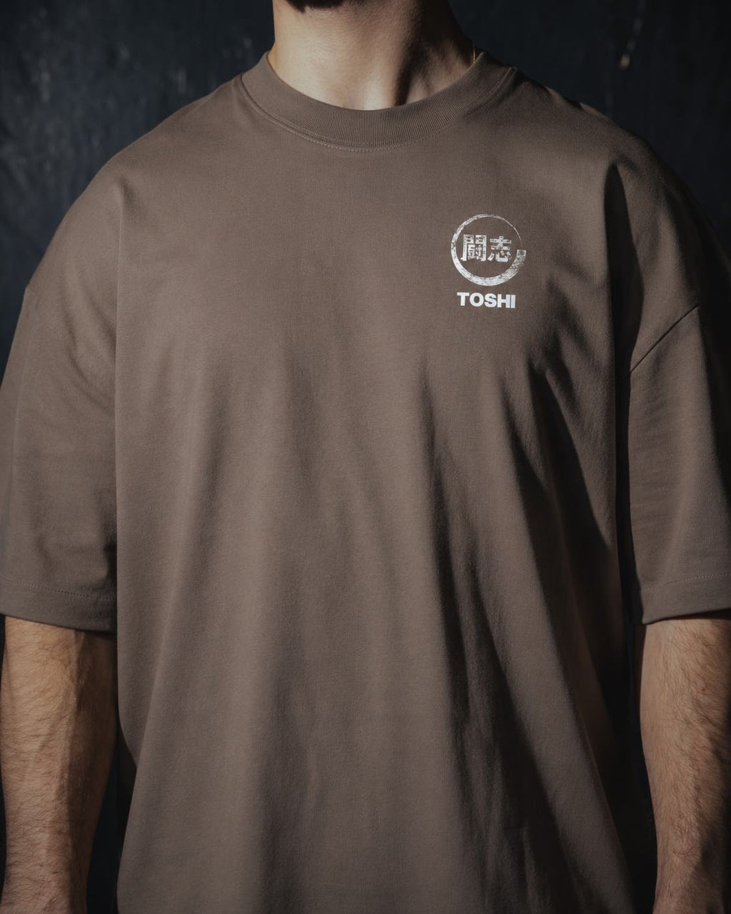 Homme de face portant un t-shirt oversize de couleur mocha, avec un logo japonais de la marque TOSHI inspiré des mangas et animes.