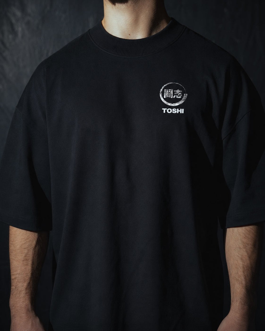 Homme de face portant un t-shirt oversize de couleur noire, avec un logo japonais de la marque TOSHI inspiré des mangas et animes.