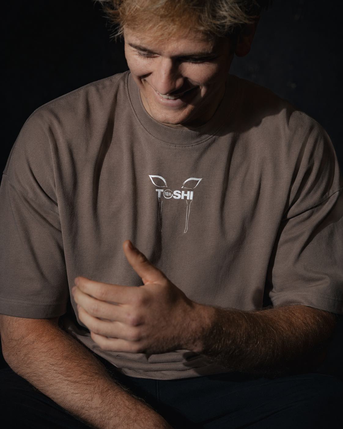 Homme de face portant un t-shirt oversize de couleur mocha, avec un logo japonais de la marque TOSHI inspiré de l'anime demon slayer.
